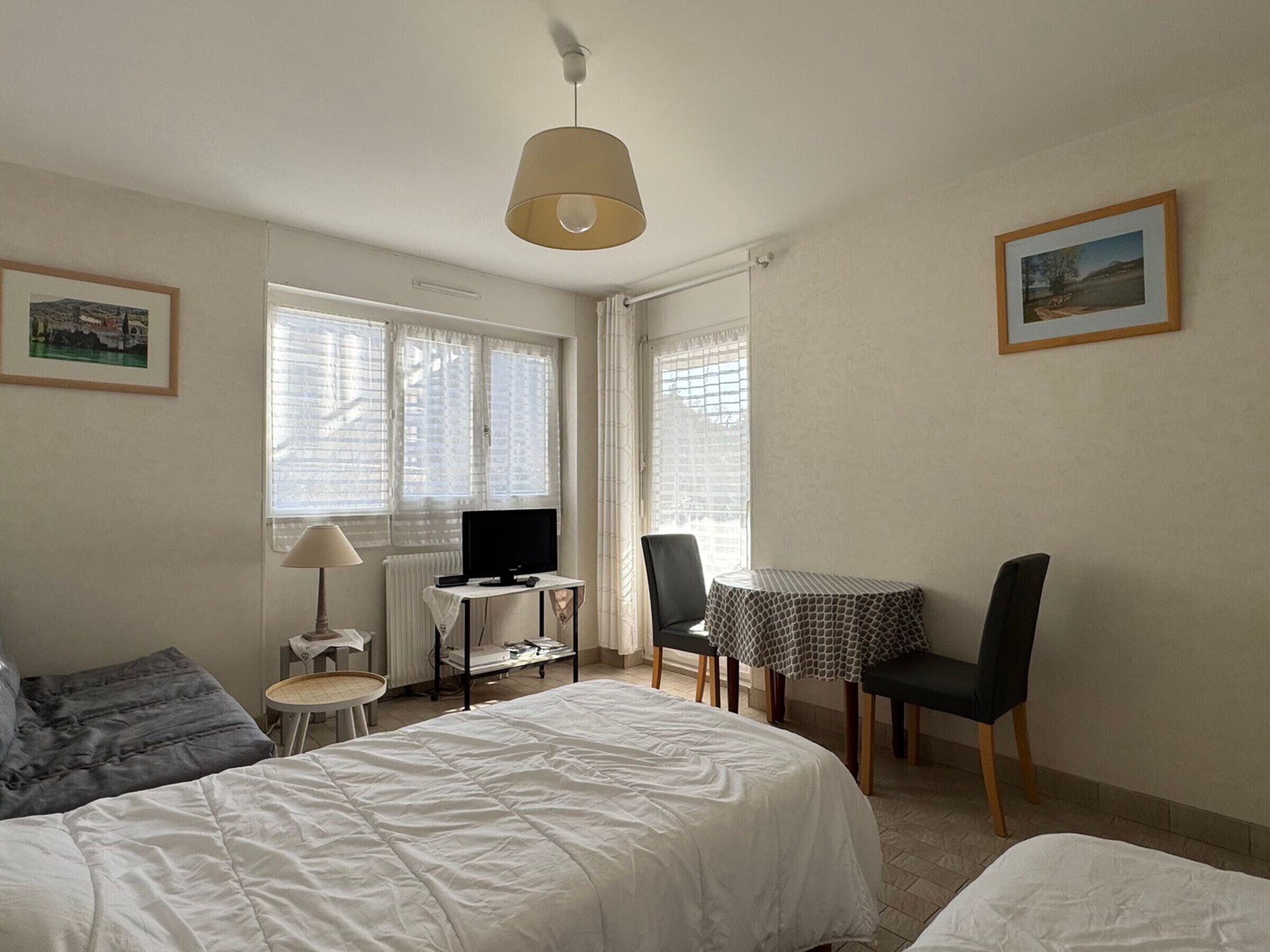 A hotel room with a bed, a desk with a computer, a chair, a table, and a lamp.