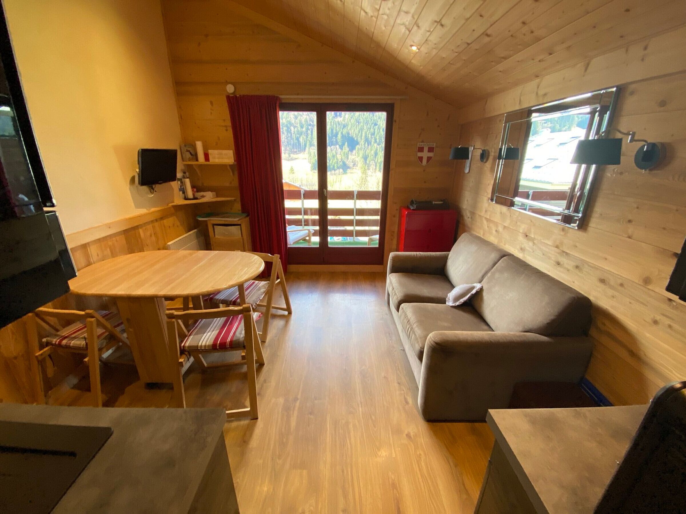 A cozy room with a wooden interior, a dining table with chairs, a sofa, and a television.