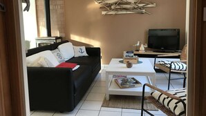 Ein Wohnzimmer mit schwarzem Sofa, weißem Couchtisch, Fernseher und Kamin.