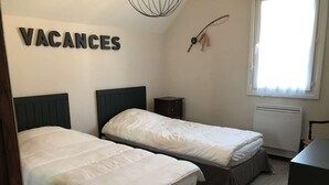 Ein Zimmer mit zwei Betten, einem kleinen Nachttisch, einem Heizkörper und einem Fenster mit Vorhängen.