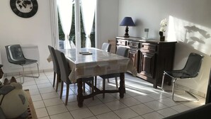 Ein Essbereich mit Tisch und Stühlen, eine Küchenzeile mit Schränken und einer Lampe sowie ein Fenster mit Vorhängen.