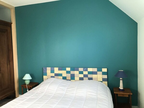 A bedroom with teal walls, a checkered headboard, a white bedspread, and two bedside tables with lamps.