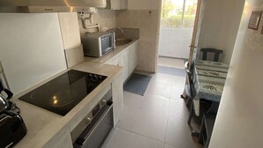 Une cuisine moderne équipée d’une cuisinière, d’un four à micro-ondes et d’un four encastrés. On y trouve un petit évier et une fenêtre qui laisse entrer la lumière naturelle.
