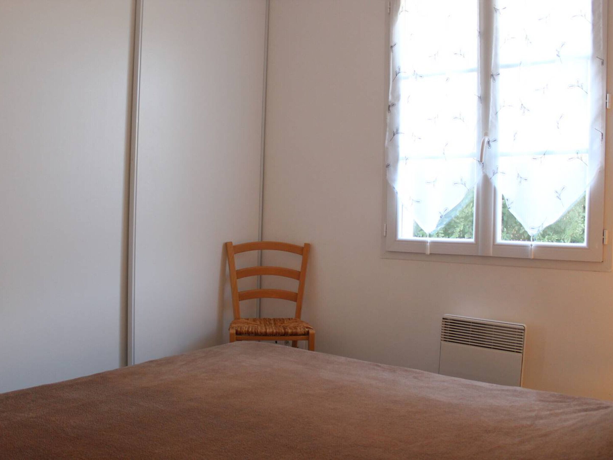 A bedroom with a single bed, a chair, a radiator, and a window with curtains.
