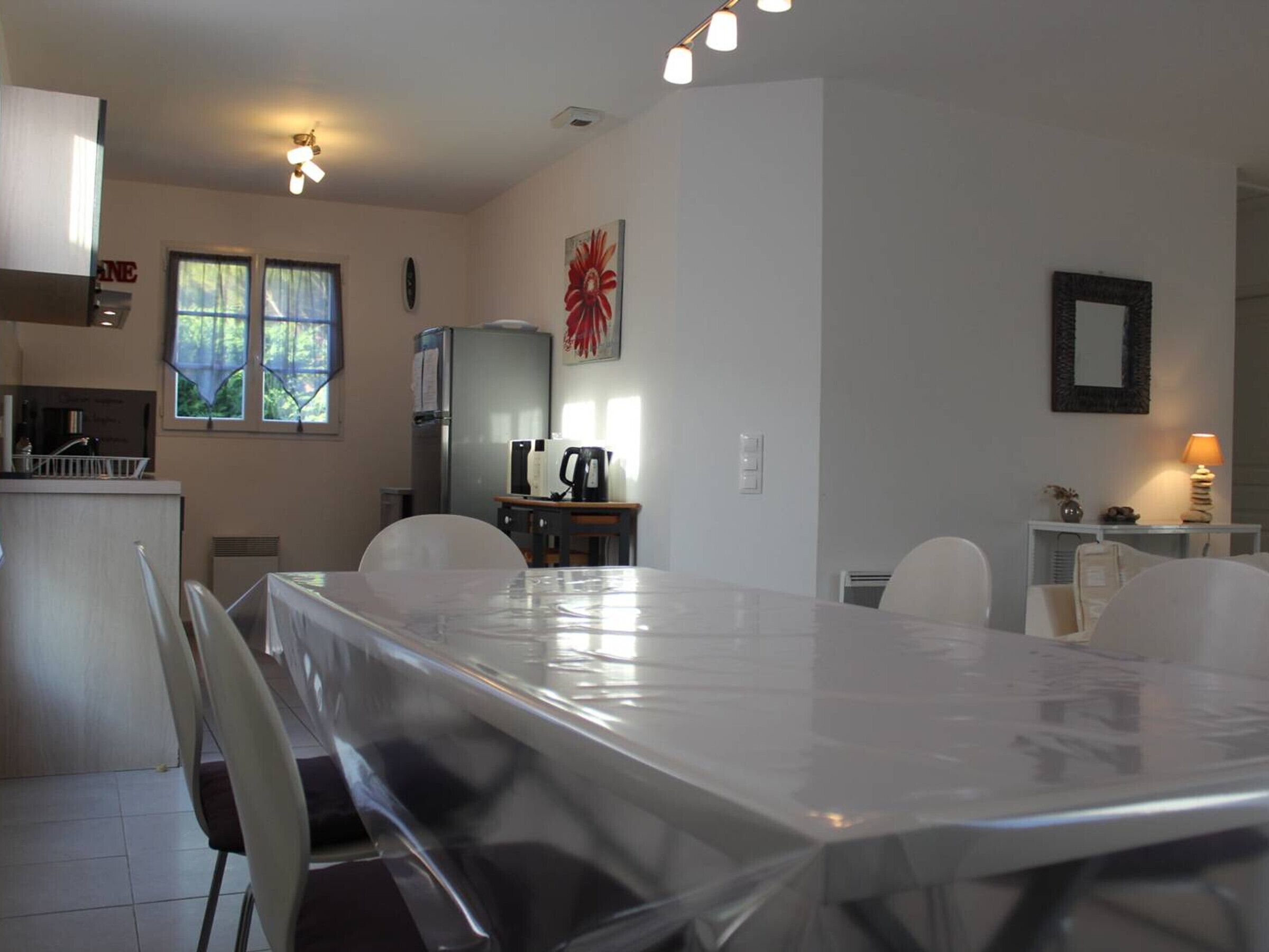 A dining area with a large table, chairs, a refrigerator, a coffee maker, and a window with curtains.