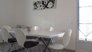A modern dining area with a white table and chairs, a ceiling light fixture, and a large window with curtains.