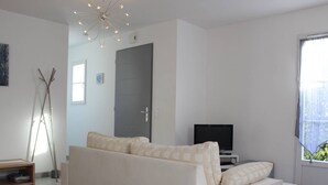 A modern living room with a white sofa, a television, and a door leading to another room.