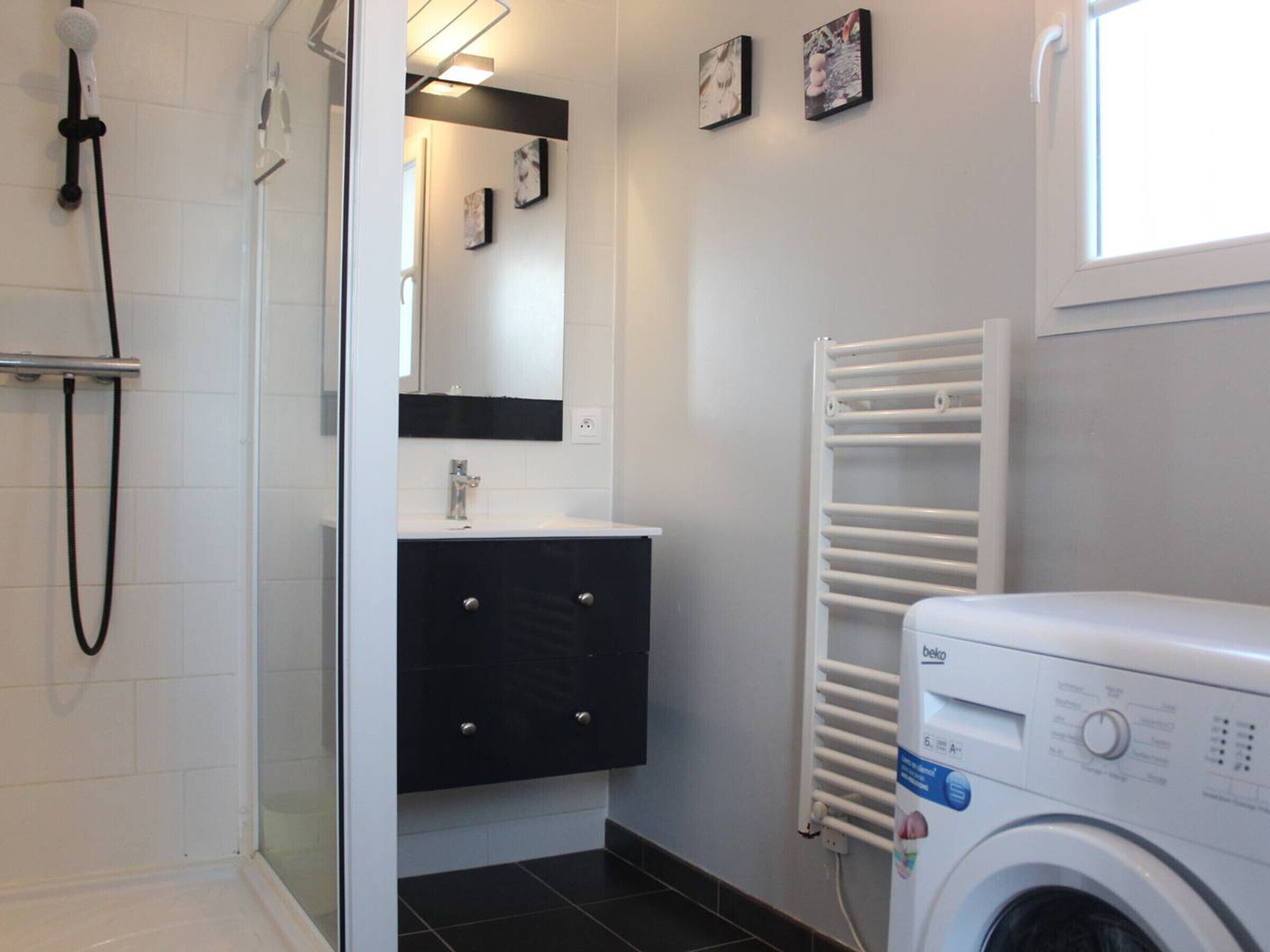 A modern bathroom with a shower, a sink, a mirror, a towel rack, and a washing machine.
