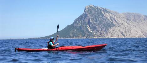A person kayaking on a calm sea with a mountain in the background.