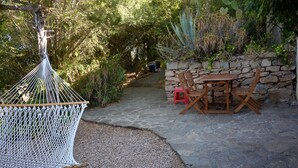 A hammock, a stone wall, and a wooden table with chairs in a garden setting.