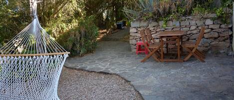 A hammock, a stone wall, and a wooden table with chairs in a garden setting.