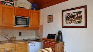 A small kitchenette with wooden cabinets, a microwave, a coffee maker, and a refrigerator. - Charming apartment near center and cable car with parking (Châtel)