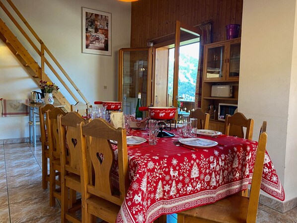 A dining area with a red tablecloth, wooden chairs, a wooden staircase, and a view of a mountainous landscape. - Spacious apartment with mezzanine near Châtel center (Châtel)