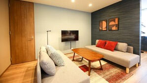 A modern living room with a sofa, a coffee table, and a flat-screen TV mounted on the wall. - PrimeRoomBeppu Hamawaki (Beppu)