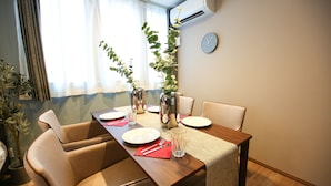 A dining table set with plates, cutlery, and glasses, surrounded by cushioned chairs, with a potted plant and an air conditioning unit in the background. - PrimeRoomBeppu Hamawaki (Beppu)