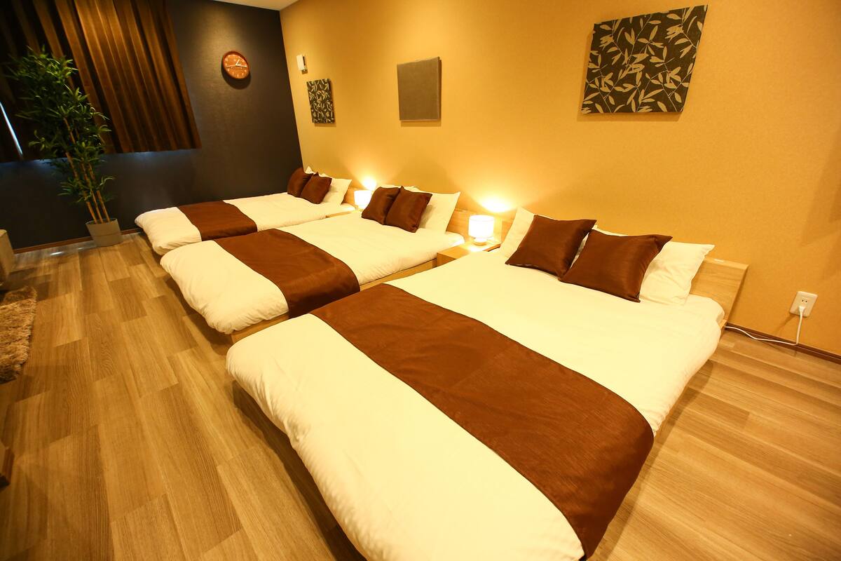 Quarto de hotel com três camas, um vaso de planta e um relógio na parede.