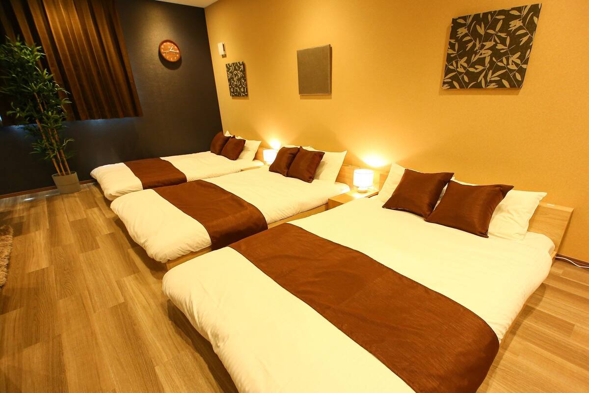 Quarto de hotel com quatro camas, um relógio, obras de arte na parede e uma planta.