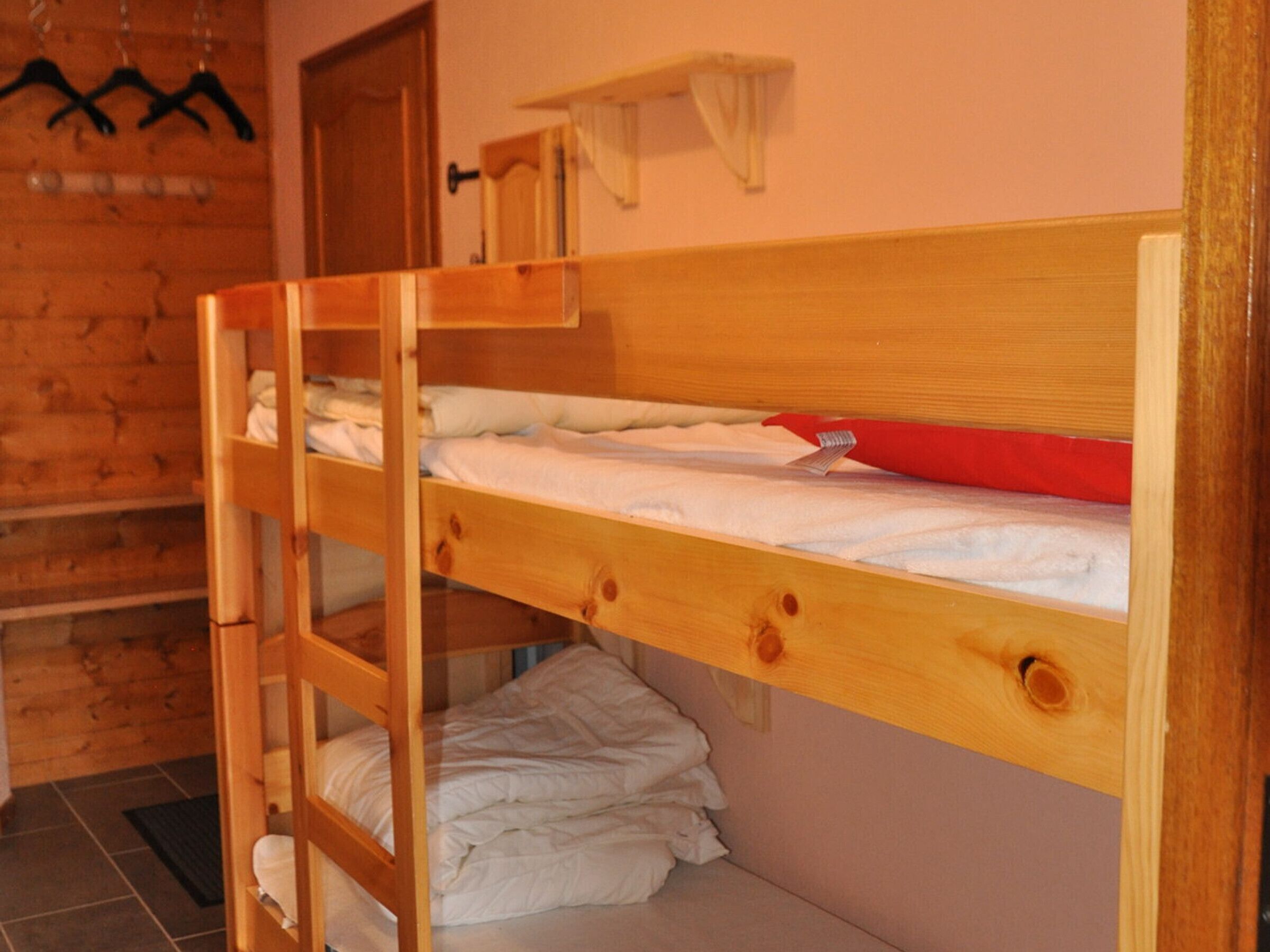 A bunk bed with a ladder, a red object on the top bunk, and a wooden wall with a door.