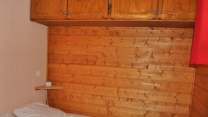 Makuuhuoneessa on puinen sängynpääty, valkoisilla vuodevaatteilla varustettu sänky ja pieni hyllykkö.