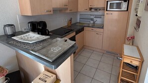 Eine kompakte Küche mit hellen Holzschränken, einer Mikrowelle, einer Kaffeemaschine und einem kleinen Holztisch.