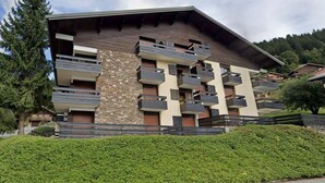 Un edificio moderno con fachada de piedra, varios balcones y un seto cuidado.