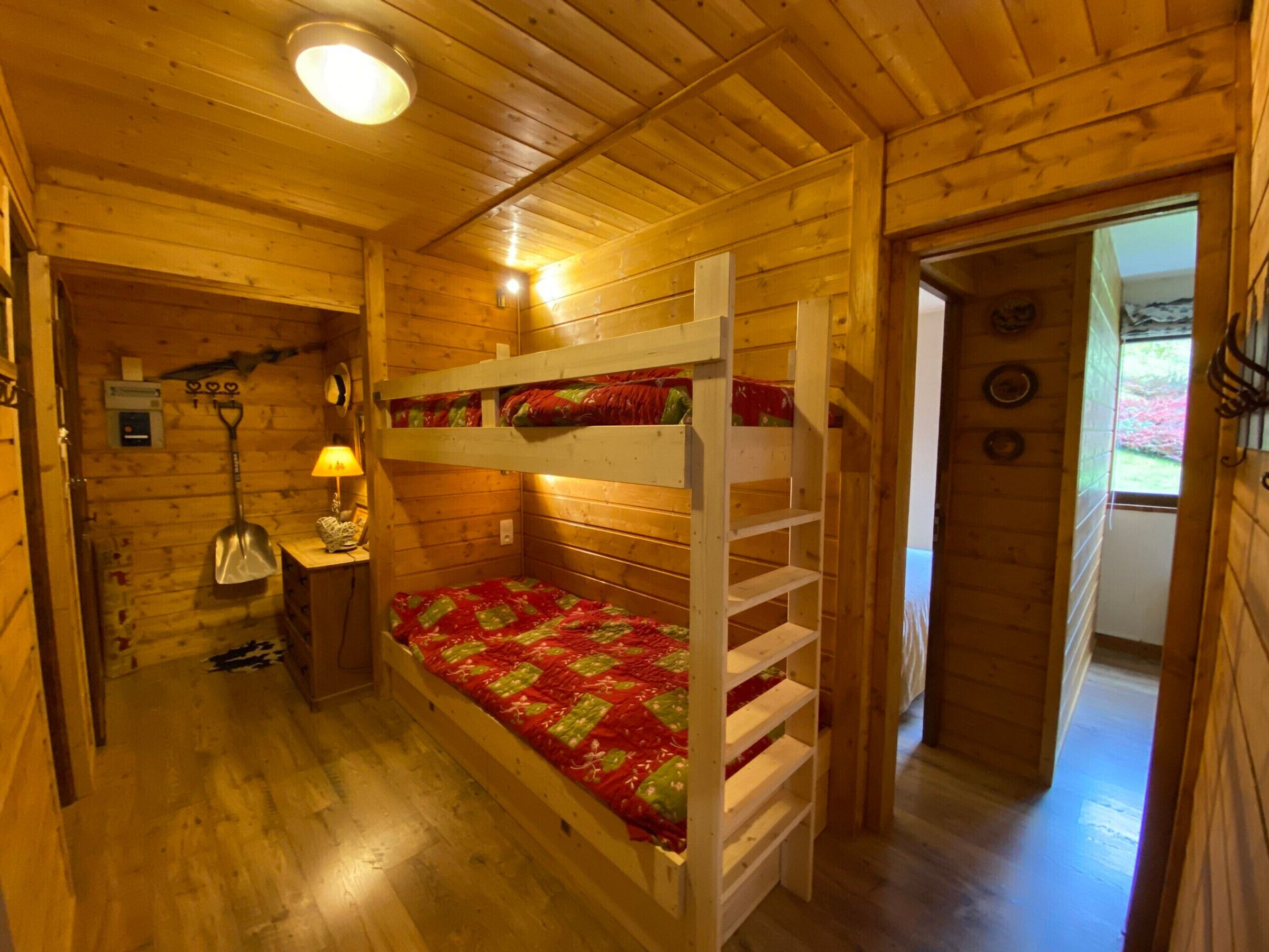 Une chambre confortable dans un chalet, avec un lit superposé, un petit bureau avec une lampe et une porte donnant sur une autre pièce.