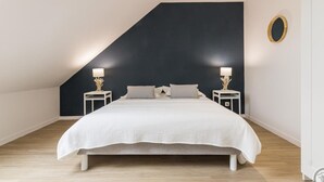 Ein modernes Schlafzimmer mit schrägem Dach, einem großen Bett, zwei Nachttischen mit Lampen und einem runden Spiegel an der Wand.