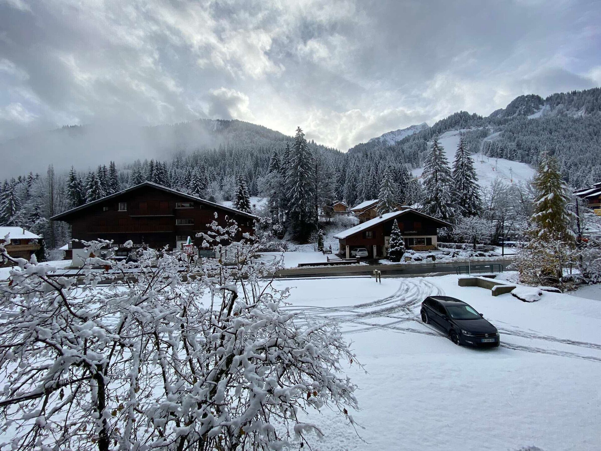 A snow-covered mountain lodge with multiple buildings, a ski lift in the background, and a car parked in the driveway.