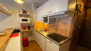 A compact kitchen with white cabinets, a microwave, a stove, and a sink. - Cozy studio with balcony and WIFI near Linga slopes (Châtel)