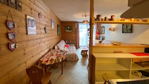 A cozy room with wooden walls, a bed, a table, and a kitchen area. - Cozy studio with balcony and WIFI near Linga slopes (Châtel)