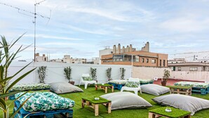 A rooftop terrace with multiple seating areas, including sofas and chairs, arranged on artificial grass.