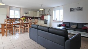A modern living room with a sofa, dining table, chairs, and a kitchen area with cabinets and appliances. - Restored Traditional House - Pets Allowed, WIFI, Enclosed Garden (Landisacq)