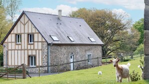A stone farmhouse with a sloped roof, a wooden fence, and a grassy field with two goats. - Restored Traditional House - Pets Allowed, WIFI, Enclosed Garden (Landisacq)