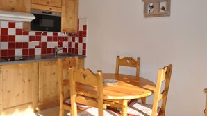 A kitchen with wooden cabinets, a red and white tiled backsplash, a microwave, and a wooden dining table with chairs. - Cozy apartment near slopes with balcony and parking (Châtel)
