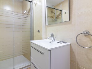 Une salle de bain moderne avec une douche à parois de verre, un lavabo blanc doté d’un robinet chromé et un porte-serviettes mural.