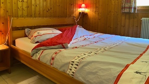 Una habitación con paneles de madera, una cama, una lámpara de pared y un ventanal con cortinas estampadas.