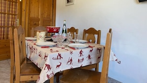 Mesa de comedor dispuesta con platos, vasos y una botella, rodeada de sillas de madera.