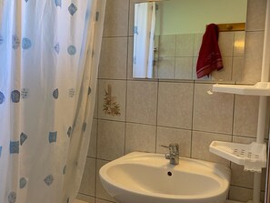 Une salle de bain avec un lavabo blanc, un miroir, un rideau de douche à motifs et une serviette rouge accrochée au mur.