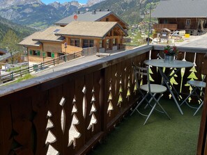 Un balcon en bois offrant une vue sur une chaîne de montagnes, une petite table avec des chaises et une clôture en bois ornée de motifs décoratifs.