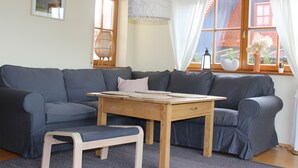 A modern living room with a grey sofa, a wooden table, and a small wooden stool. - Place in the sun (Gräfenberg)