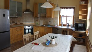 A kitchen with wooden cabinets, a refrigerator, a stove, and a dining area with a table and chairs. - Place in the sun (Gräfenberg)