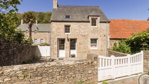 Une maison en pierre avec une porte et des fenêtres blanches, un mur de pierre à l’avant et une clôture blanche.