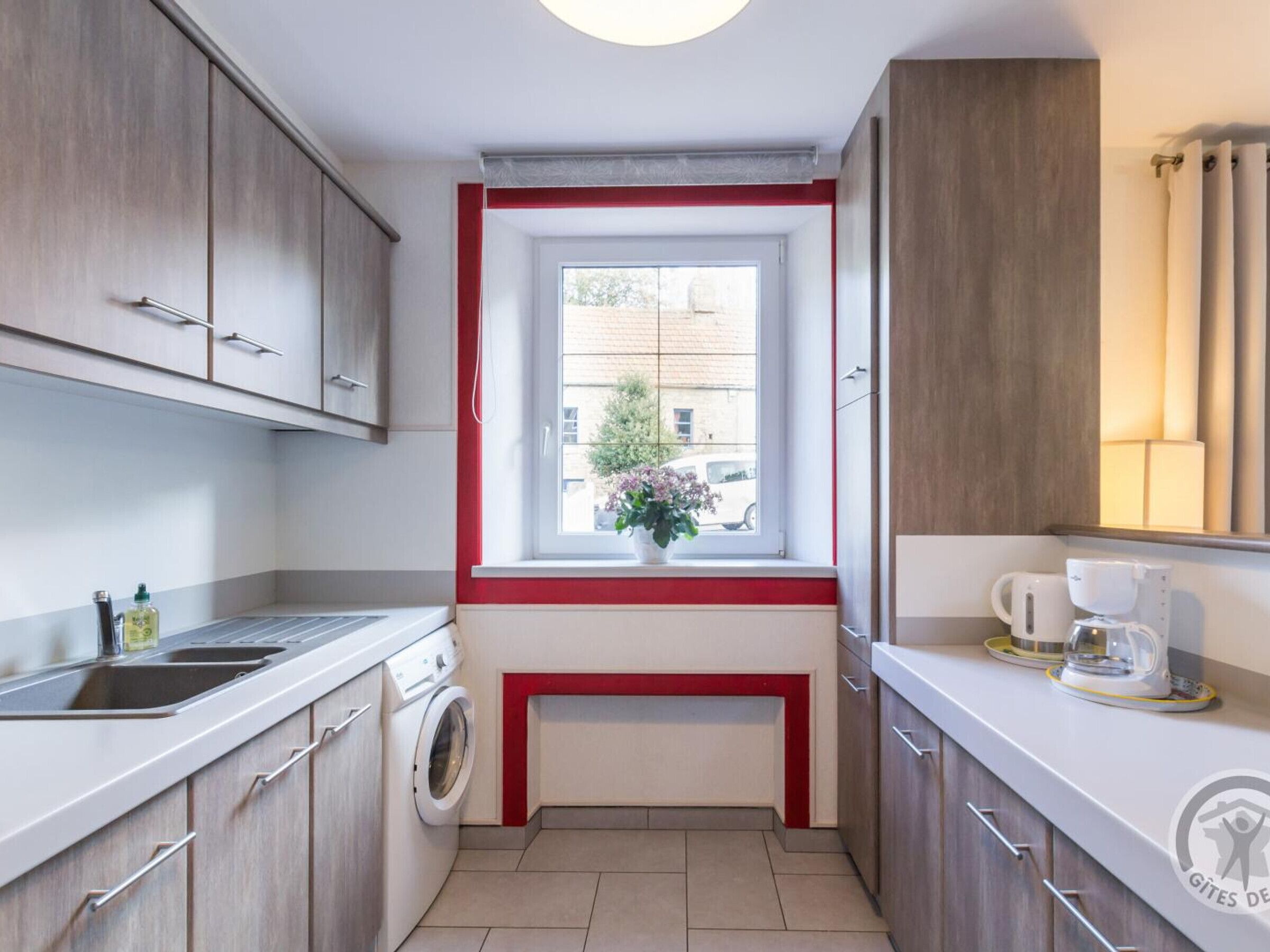 Uma cozinha compacta com máquina de lavar, pia e janela com vista para o exterior.