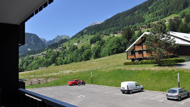 A view of a parking area with a building, a red car, and a white van. - Comfortable two-room with balcony and parking, near ski lifts (La Chapelle-d'Abondance)