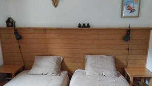 A room with two beds, wooden headboard, wall-mounted lamp, and a mounted deer head. - Comfortable two-room with balcony and parking, near ski lifts (La Chapelle-d'Abondance)