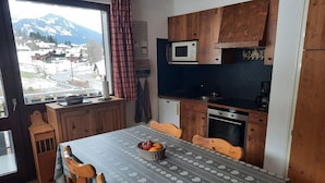 A cozy kitchen with wooden cabinets, a microwave, and a dining table with chairs. - Comfortable two-room with balcony and parking, near ski lifts (La Chapelle-d'Abondance)
