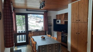 A compact kitchen with a dining table, wooden cabinets, a microwave, and a view of a snowy landscape through the window. - Comfortable two-room with balcony and parking, near ski lifts (La Chapelle-d'Abondance)