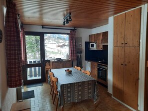 Kompakti keittiö, jossa on ruokapöytä, puukaapit, mikroaaltouuni ja ikkunasta avautuva näkymä lumiseen maisemaan.