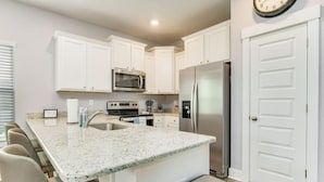 A kitchen with white cabinets, a stainless steel refrigerator, a microwave, and a granite countertop.