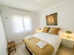 A bedroom with a large bed, two bedside tables, a small wooden stool, and a painting on the wall.